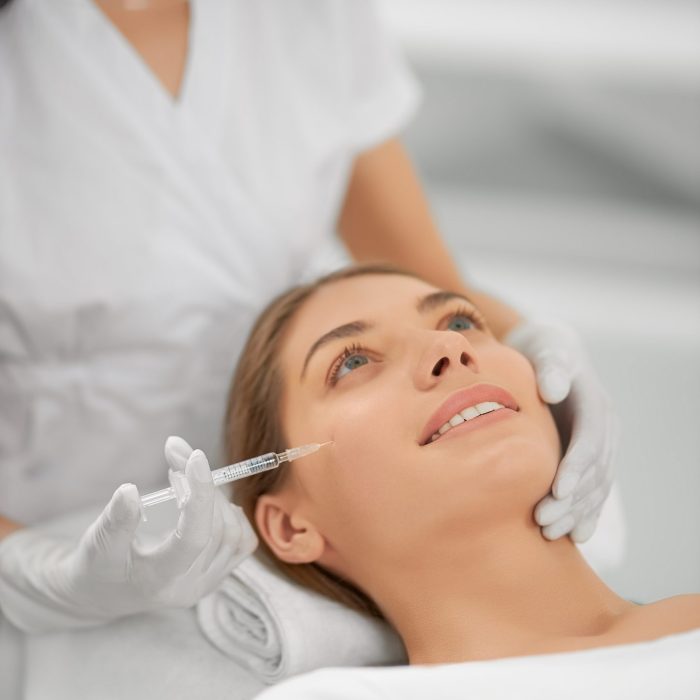 Close up of smiling young brunette woman on procedure injection anti-aging skin in beautician. Concept of process injection for improve the condition face.